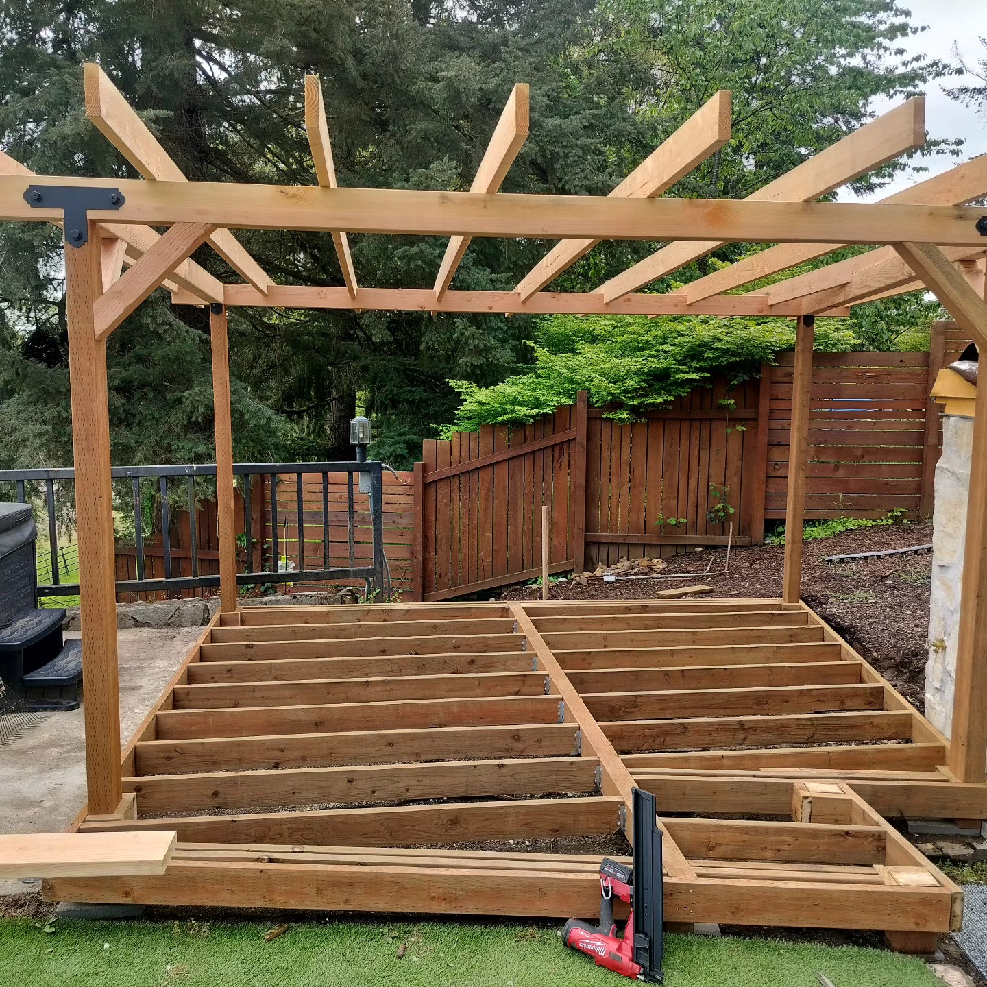 A cedar pergola and deck frame under construction in a backyard